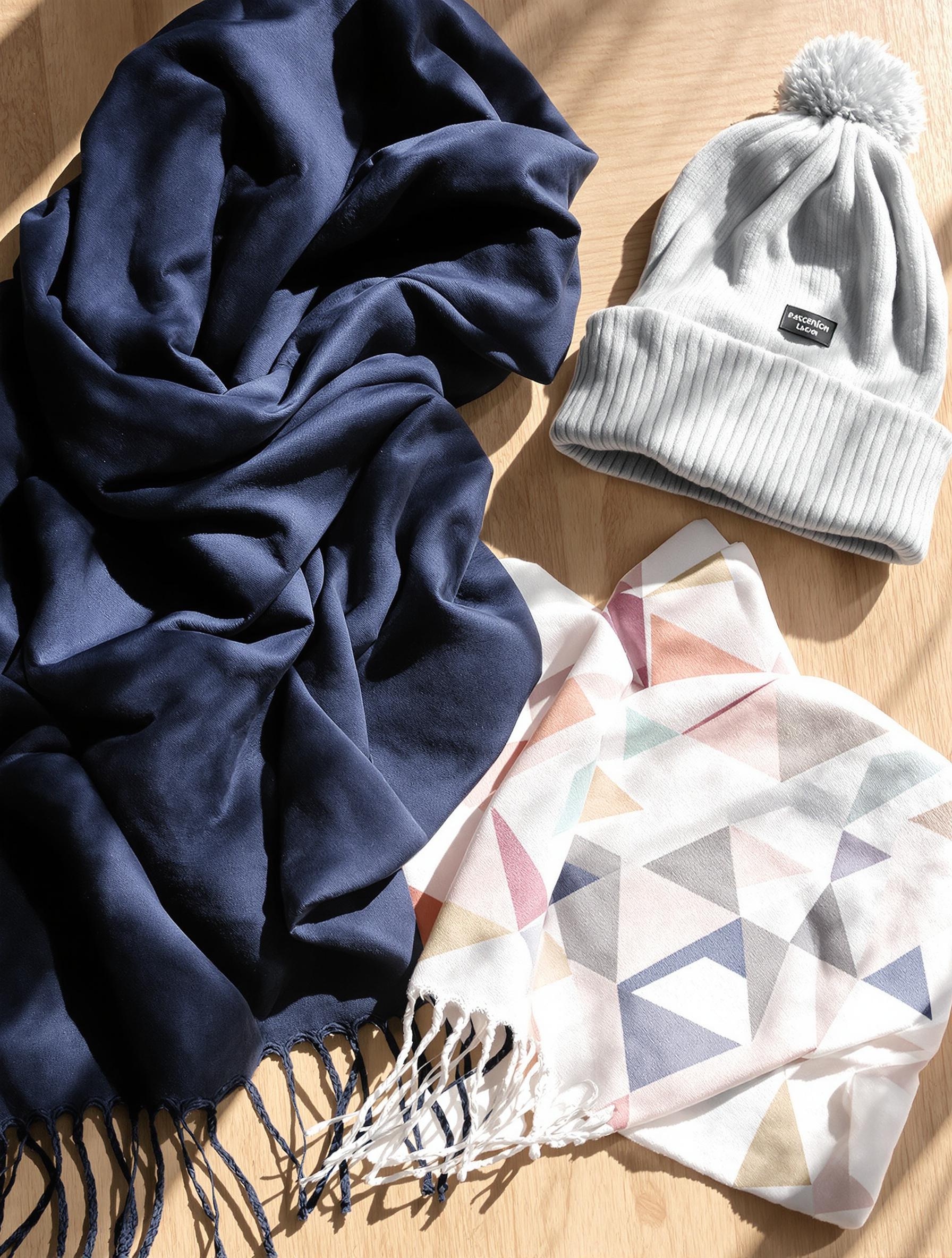 Accessoires essentiels mi-saison : châle laine marine, foulard géométrique pastel et bonnet coton gris clair alignés